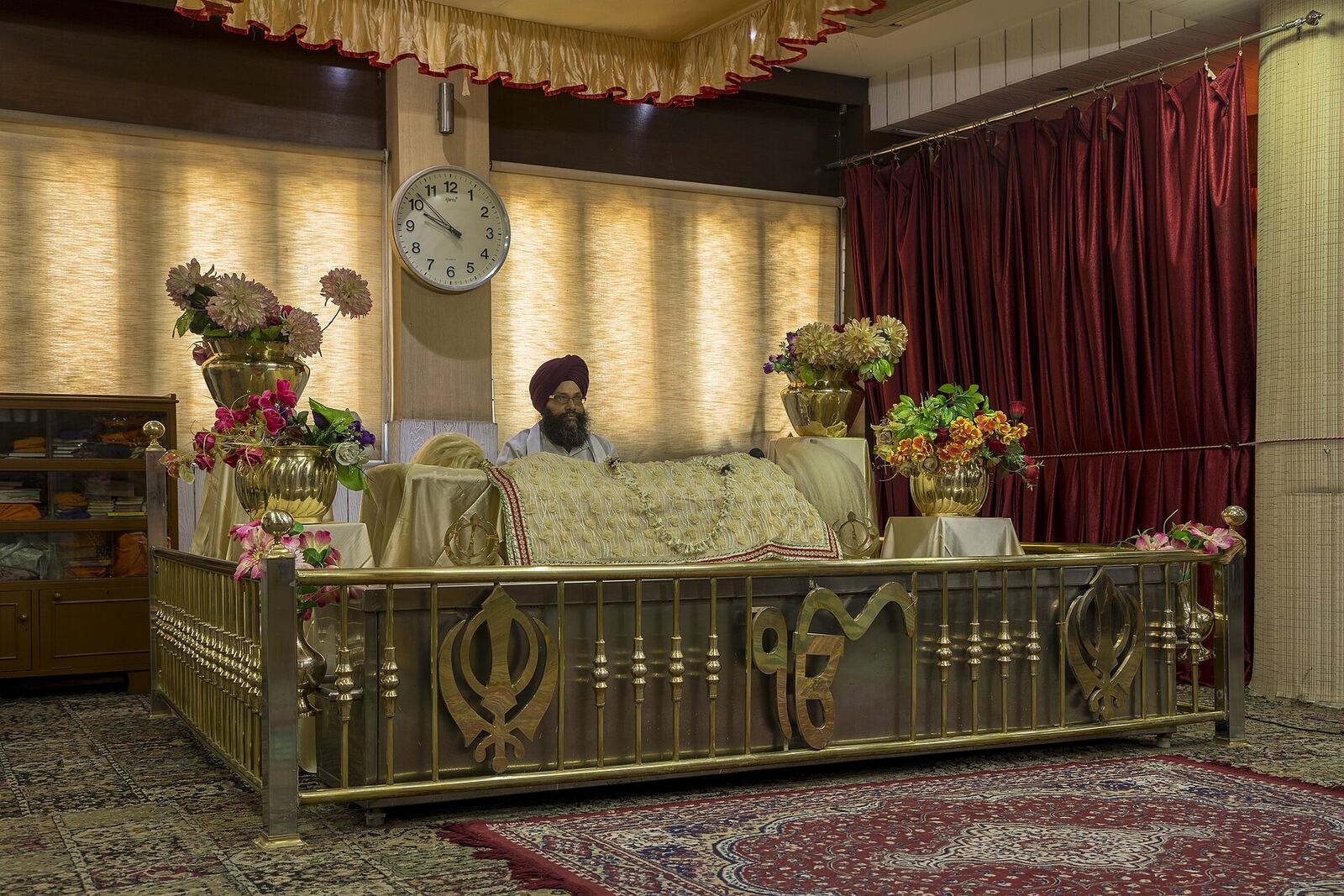 Guru Granth Sahib | Sikh Saints A Sikh man rests near a sacred scripture within a Gurdwara, showcasing spiritual devotion.