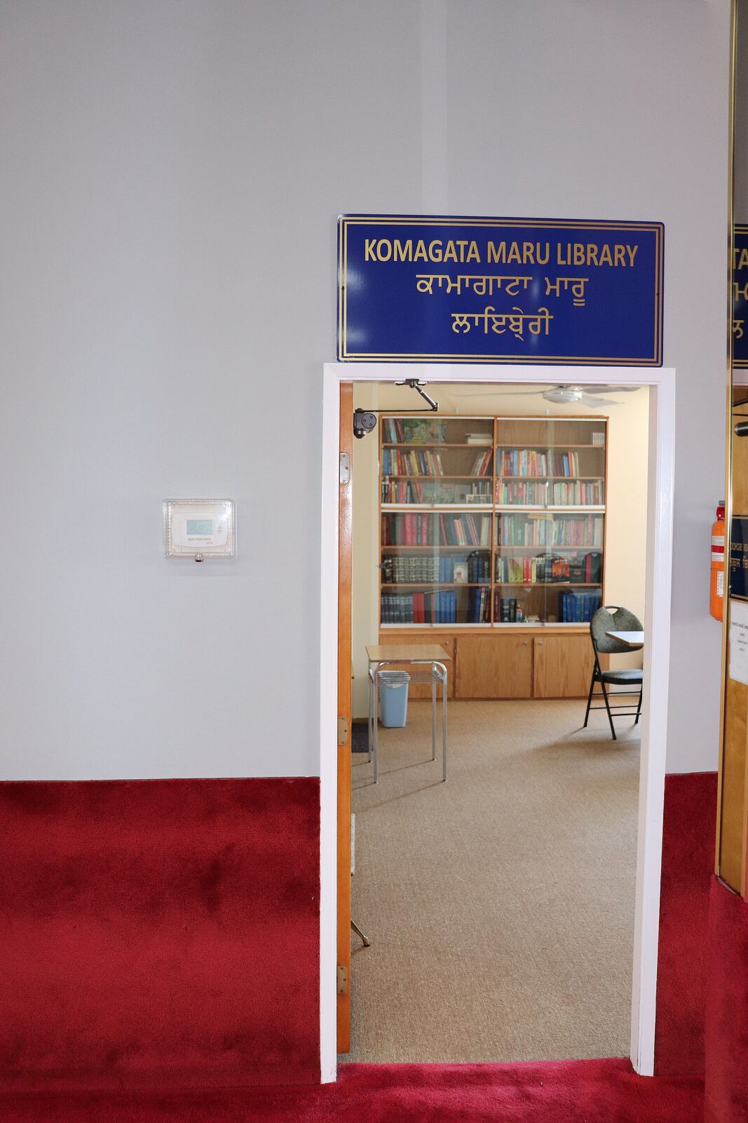 Komagata Maru Library | Sikh Saints The Komagata Maru Library has bookshelves and a red carpeted hallway, showcasing Sikh history.
